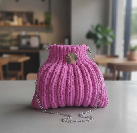 Magenta dzianinowa kopertówka ze srebrnym paskiem łańcuszkiem na białym blacie z rozmytym tłem kuchennym
